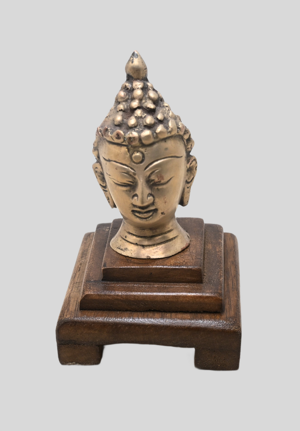 Brass meditating Buddha bust on wooden base, angled view